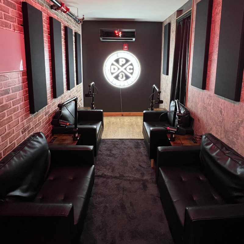 A podcast recording studio 4 chairs with microphones face each other. The Detroit Podcasting Company logo is on the back wall.